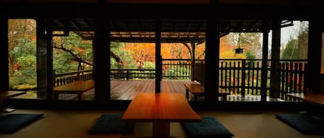 A traditional Japanese room with tatami flooring, a wooden table, and a view of autumn foliage through a sliding door.