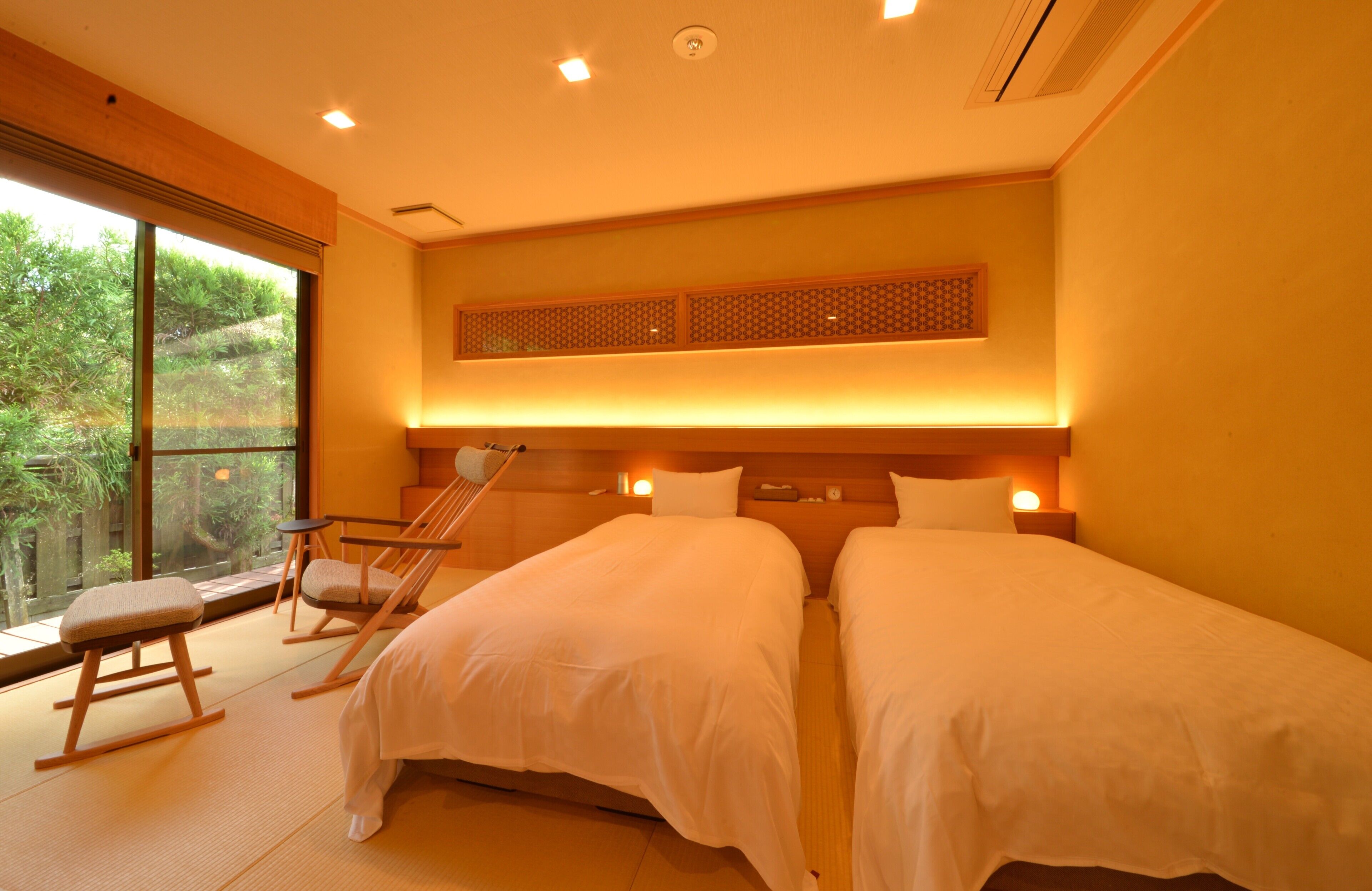 A hotel room with two beds, a large window, tatami mats, and a view of greenery.