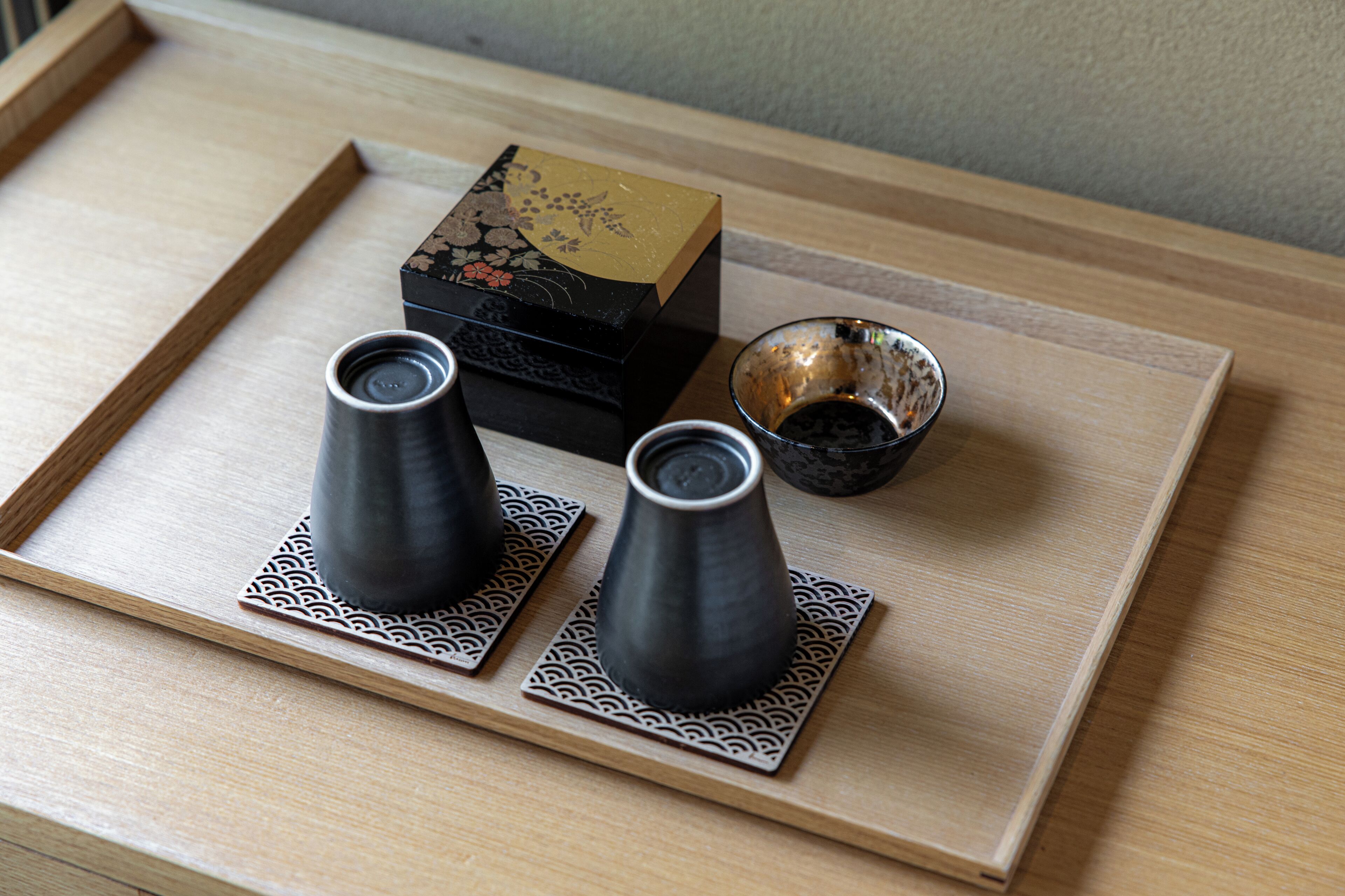 A tray with two black cups and a small bowl on a wooden tray.