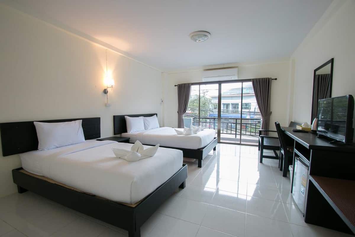 A hotel room with two beds, a desk, a television, and a balcony with curtains.