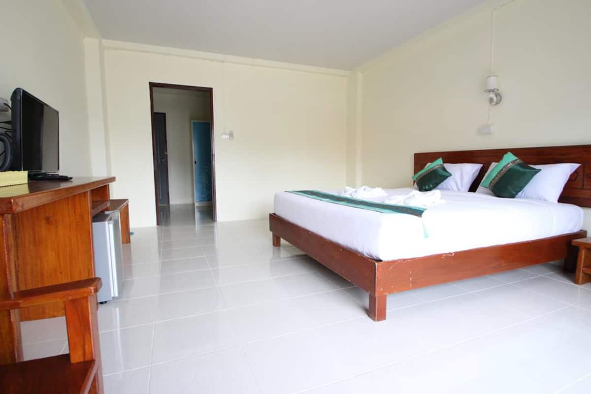 A bedroom with a wooden bed, a desk with a television, and a tiled floor.