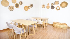 Quarto com piso de madeira, paredes brancas e uma mesa com cadeiras. Há vários cestos trançados e objetos decorativos na parede.