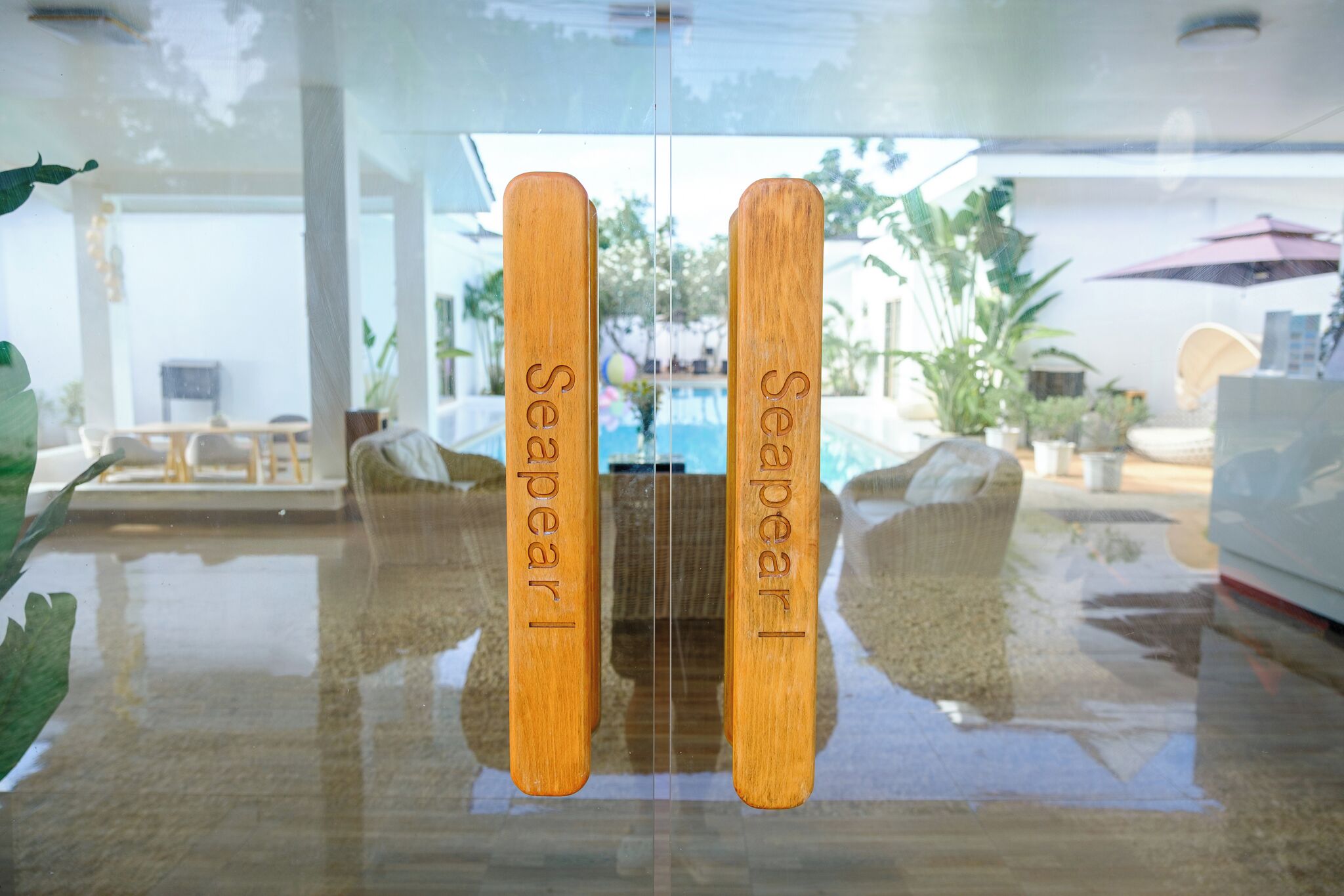 A glass partition with two wooden plaques engraved with 'Seapark' and a reflection of an outdoor seating area with a pool and umbrellas.