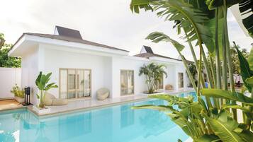 A modern house with a swimming pool, large windows, and tropical plants.