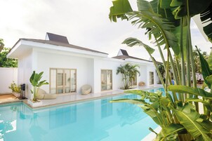 Una casa moderna con piscina, ventanas amplias y plantas tropicales.