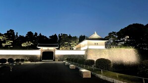 Un torii tradicional japonés con tejado de tejas, rodeado de muros de piedra y un jardín bien cuidado con setos recortados.