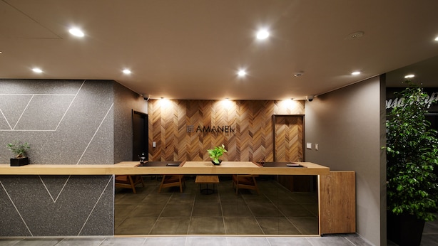 Zona de recepción con un mostrador de madera, pared con diseño de espiga y una planta en maceta.