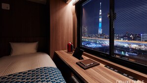 Habitación de hotel con una cama, un escritorio con una computadora portátil, una lata de bebida roja y vistas a un paisaje urbano nocturno.