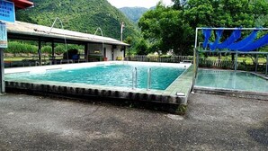 A rectangular swimming pool with a tiled deck, surrounded by a metal fence and a covered area with a roof. - Phoenix Landscaping B&B (Yuanshan)
