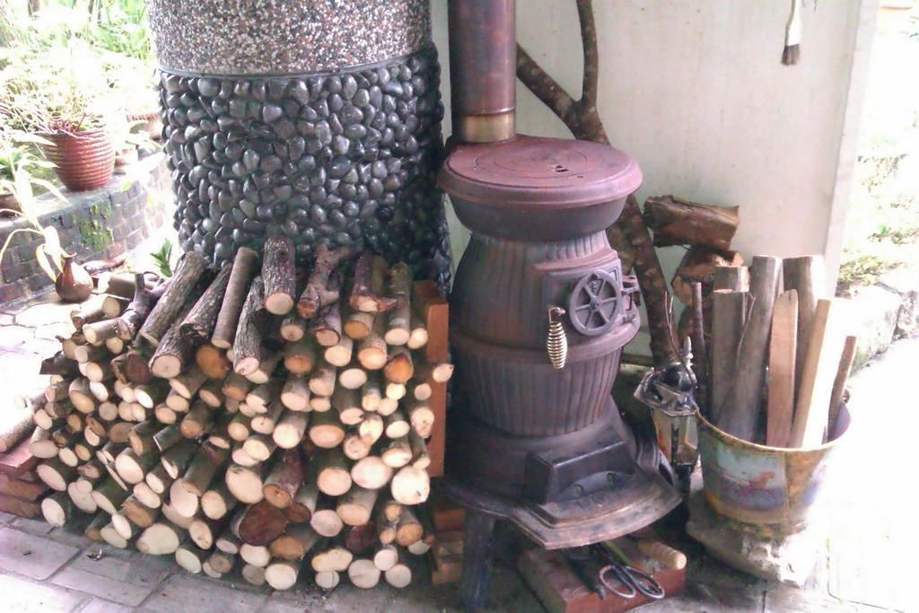A wood stove with a stone base and logs stacked beside it.