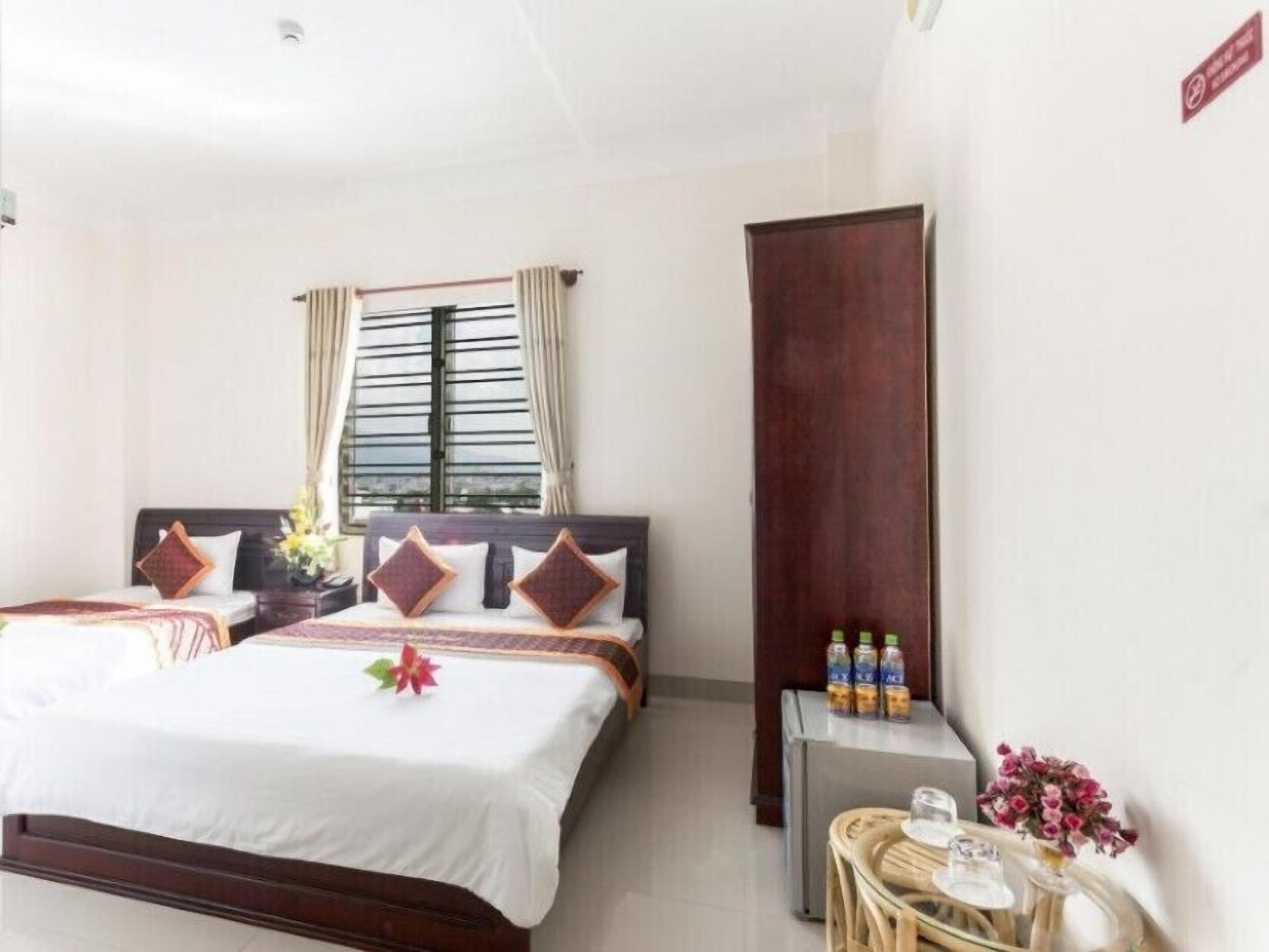 A hotel room with a bed, a small table with bottles, and a window with curtains.