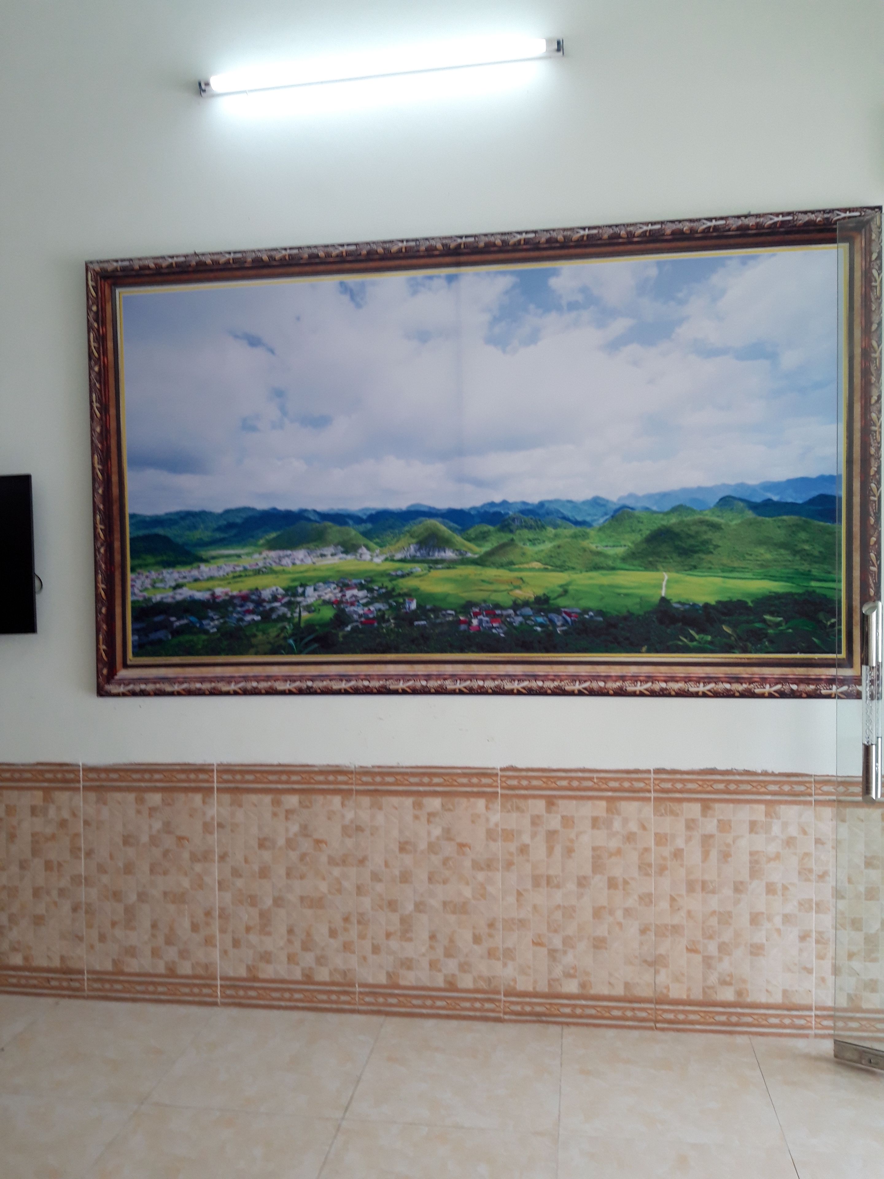 A large framed landscape painting on a wall, a tiled floor, and a light fixture above the painting.