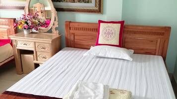 A neatly made bed with a white bedspread and a red pillow, a wooden dresser with a mirror and a vase of flowers, and a framed picture of a mountainous landscape on the wall.