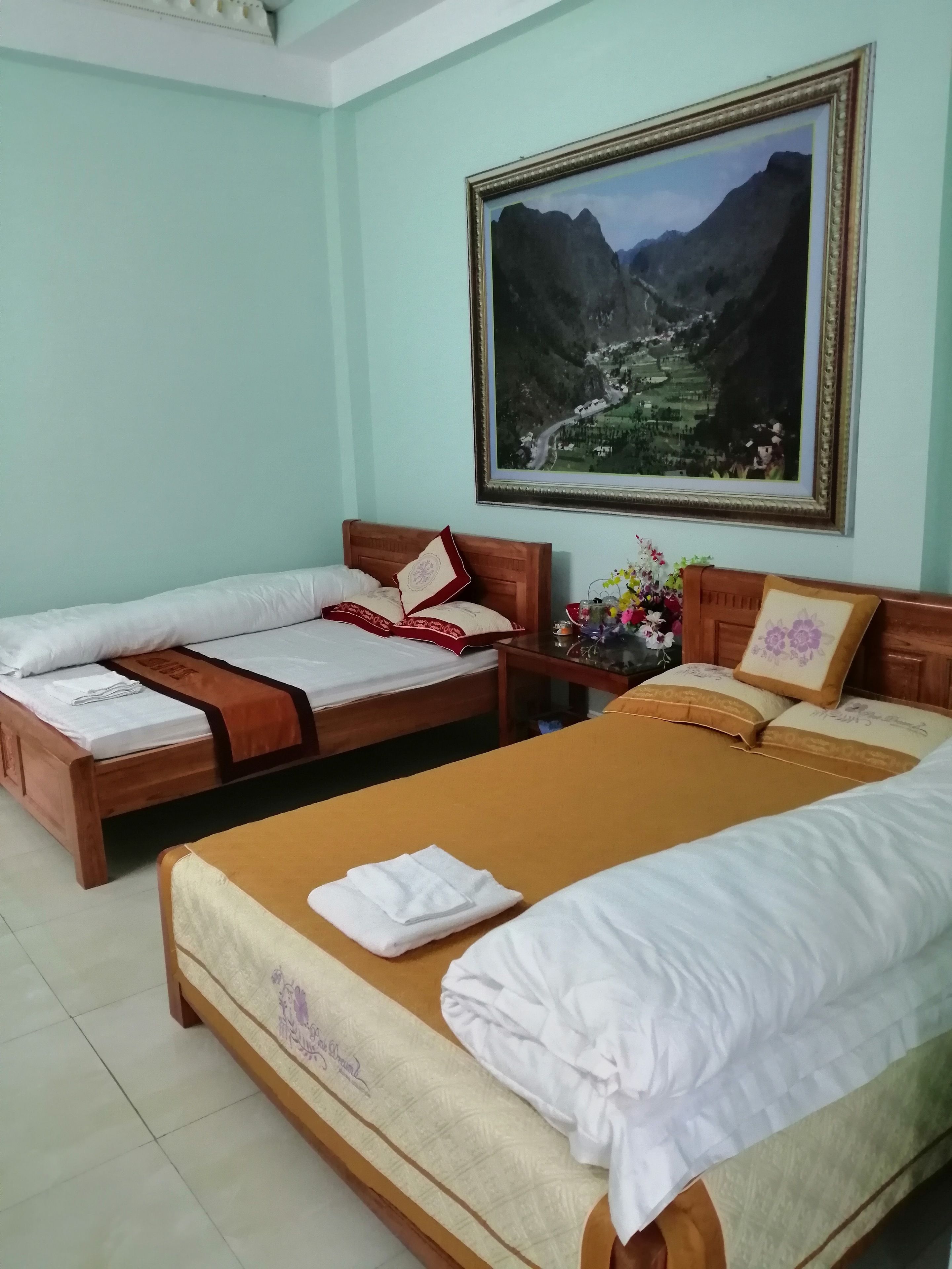 Habitación de hotel con dos camas de madera, una con cubrecama rojo y blanco estampado y la otra con cubrecama marrón. En la pared, hay una fotografía enmarcada de un paisaje montañoso.