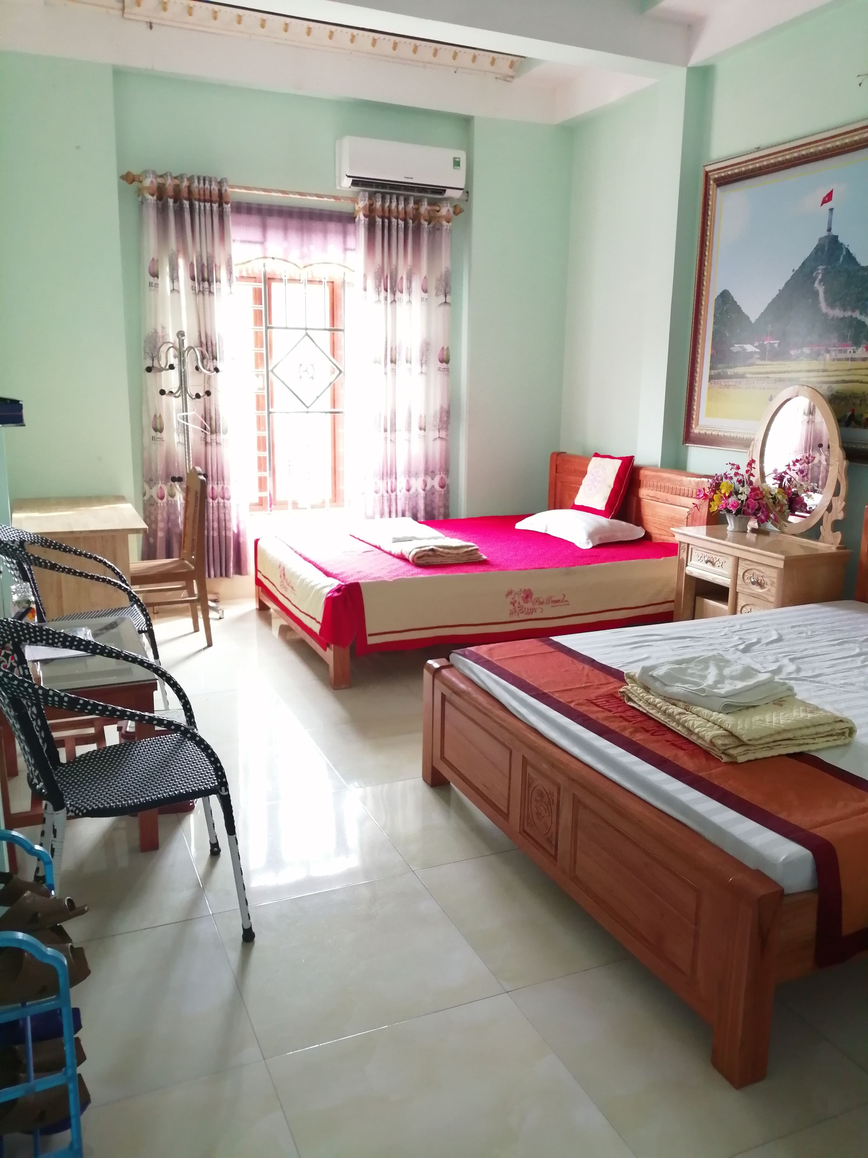 A hotel room with two beds, a wooden nightstand, a chair, and a dining area with chairs and a table.
