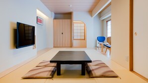 Una habitación moderna con suelo de estera de tatami, una mesa baja, un televisor y una puerta corredera que da a otra habitación.