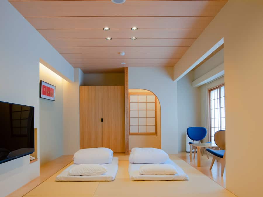 A room with two beds, a TV, a wooden wardrobe, and a window with a view.