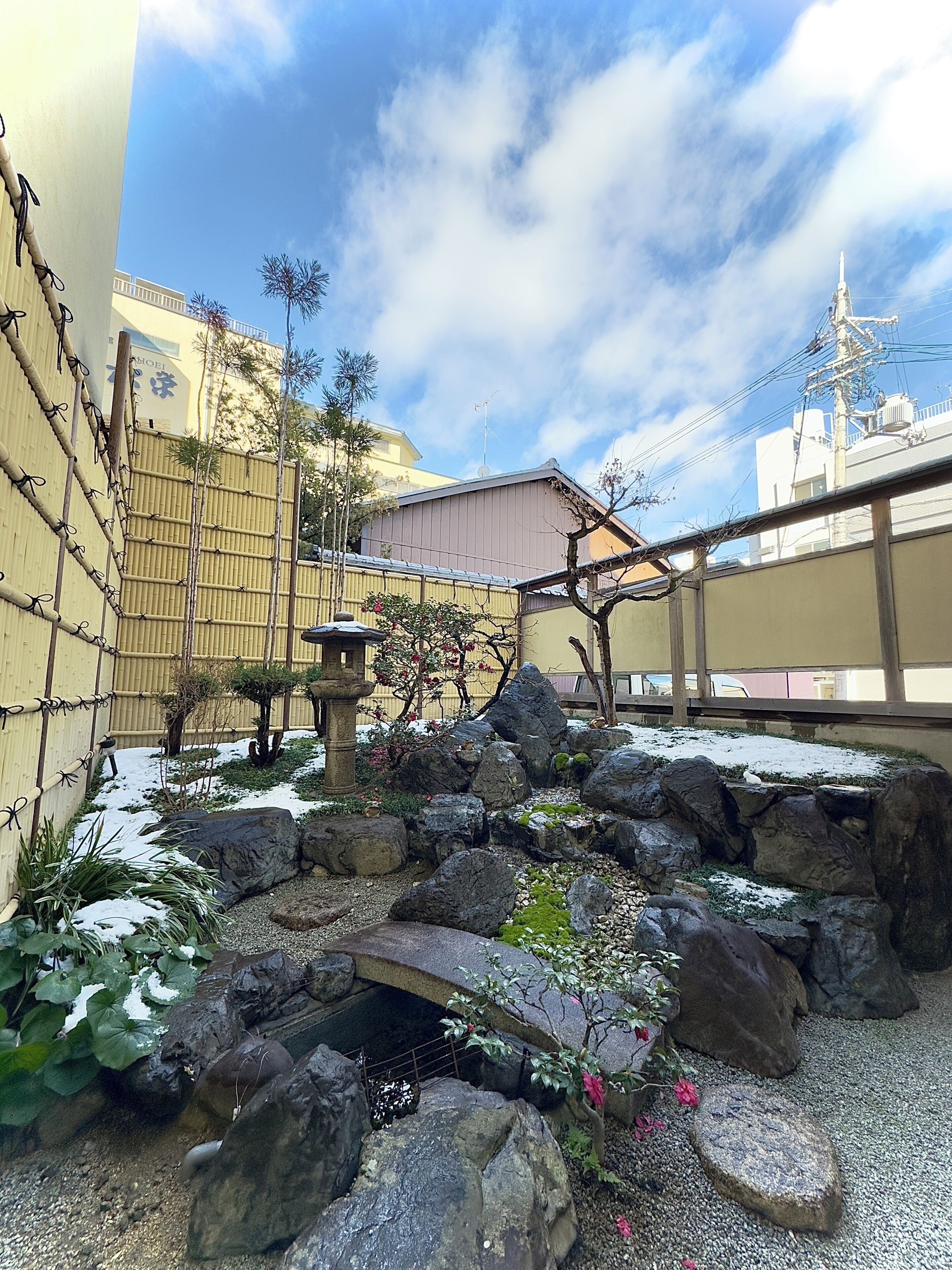 Um jardim japonês tradicional com pedras, um lampião de pedra e cerca de bambu.