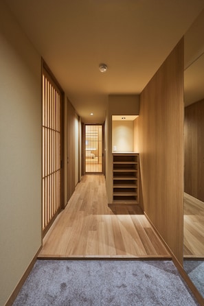 Un couloir étroit au plancher en bois, une entrée recouverte de moquette et un escalier menant à une pièce.