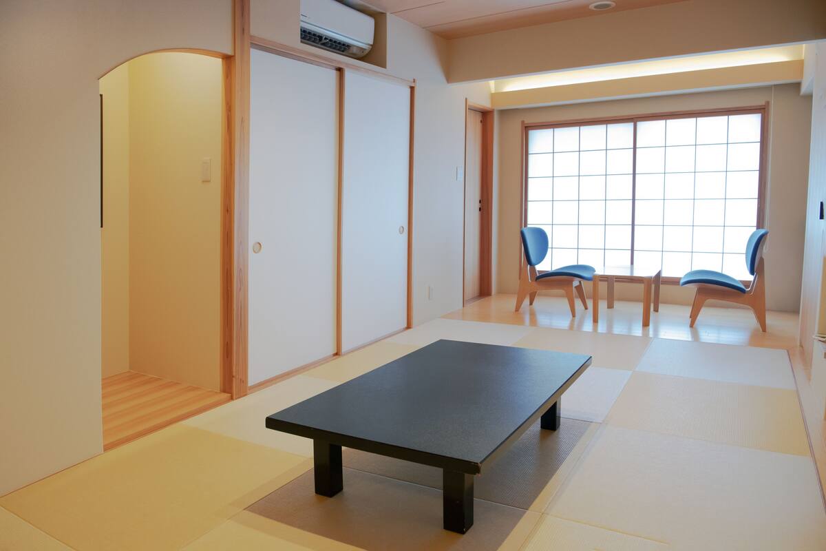 Una habitación con suelo de tatami, una mesa baja y dos sillas azules.