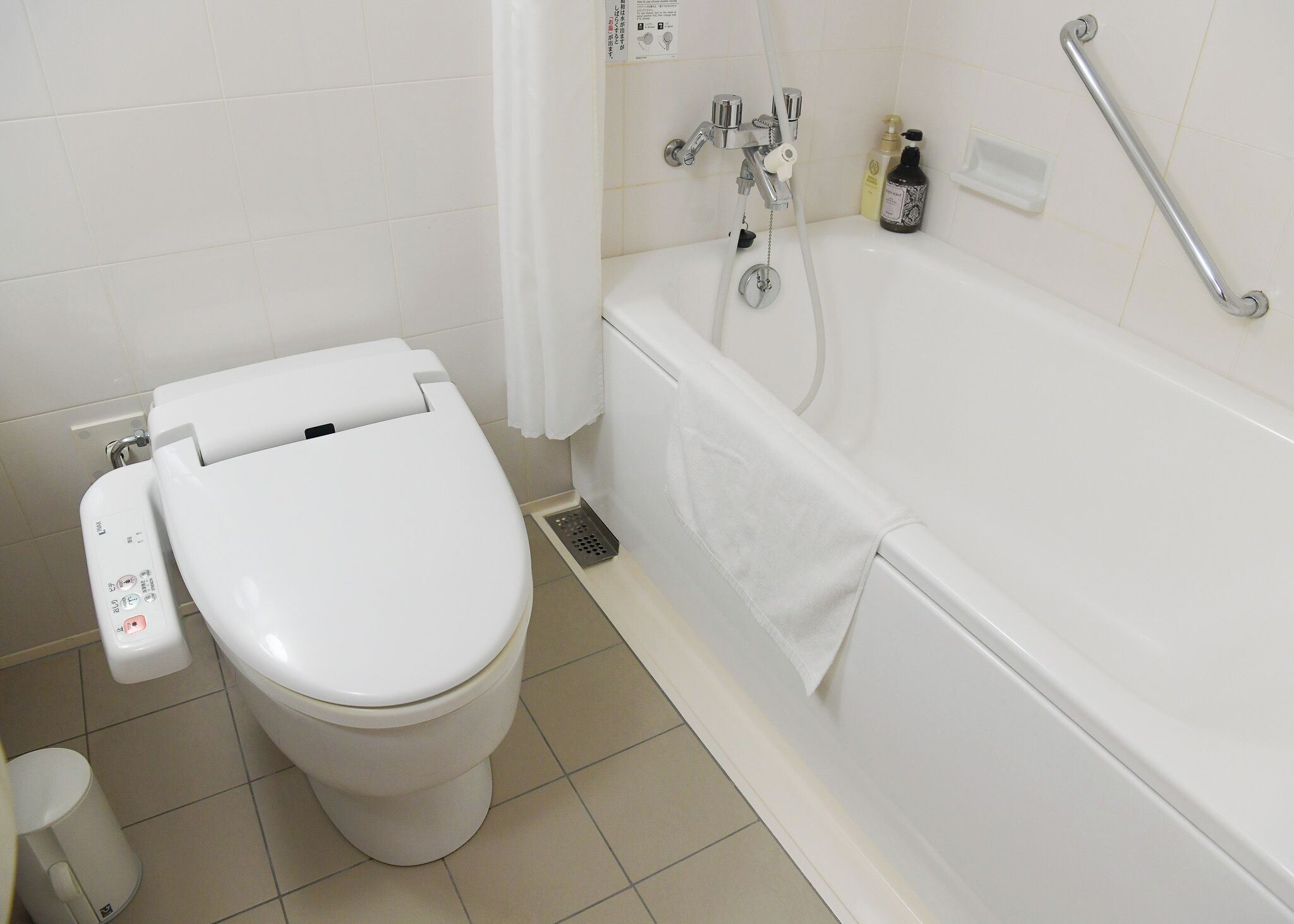 A bathroom with a white toilet, a white bathtub, and a grab bar.