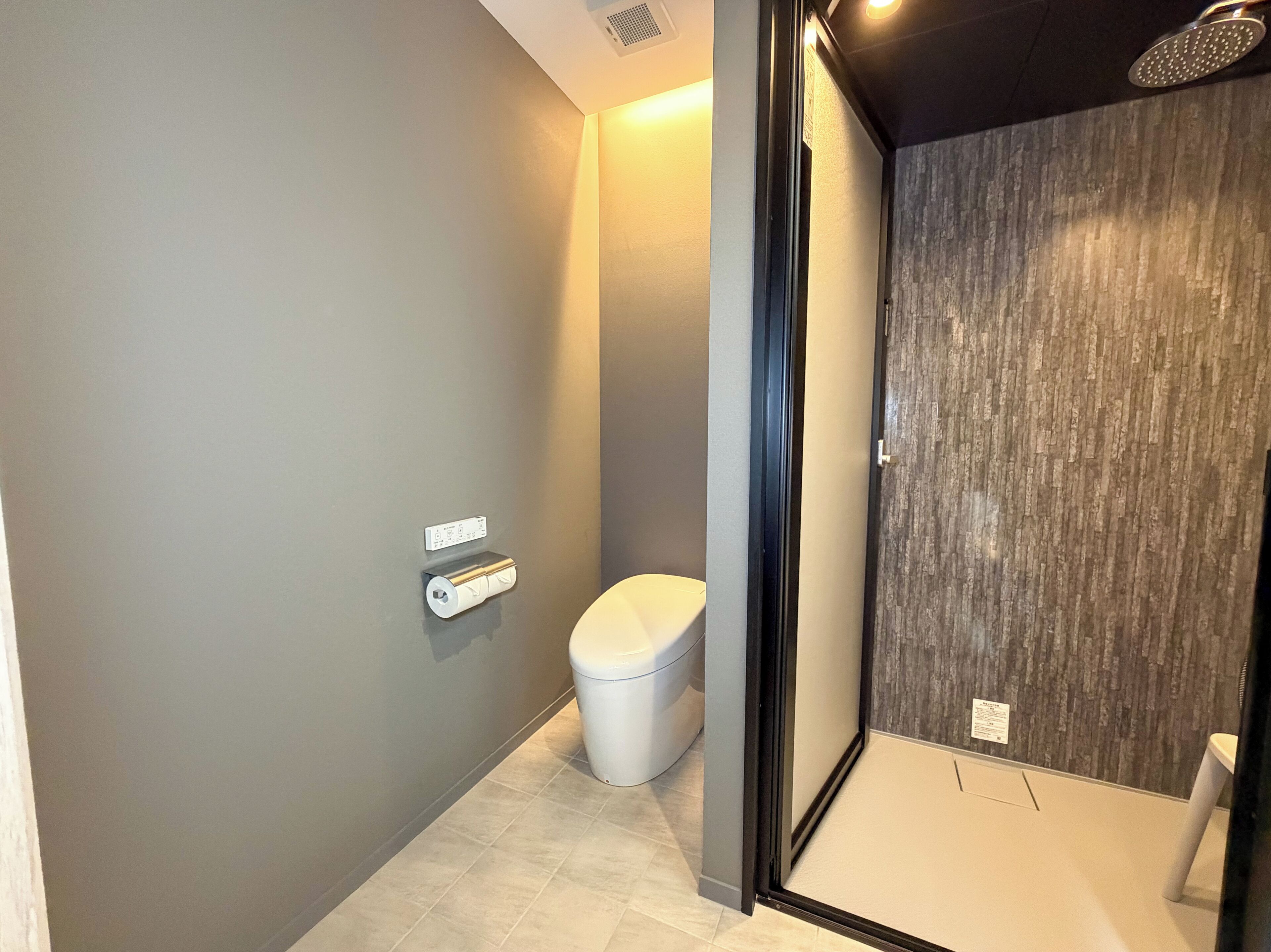 A modern bathroom with a toilet, a shower enclosure, and a towel dispenser.