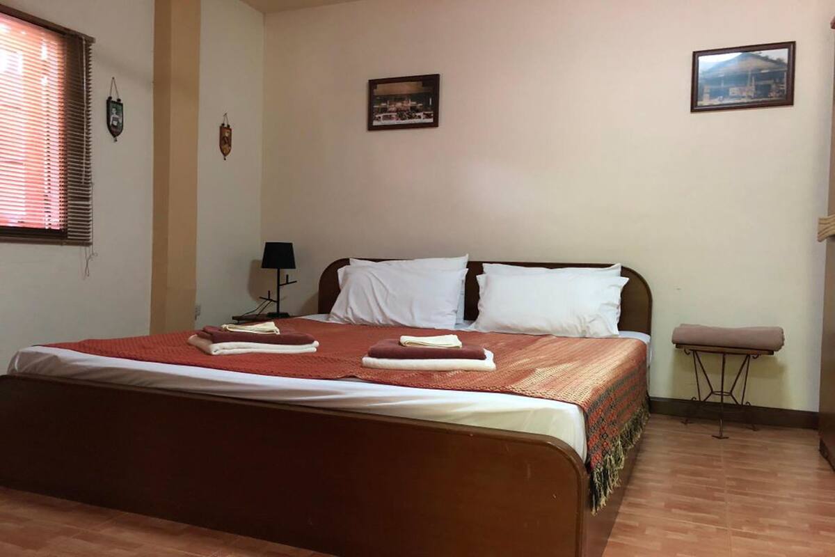 A neatly made bed with a red and white bedspread, a bedside table with a lamp, and a small stool.