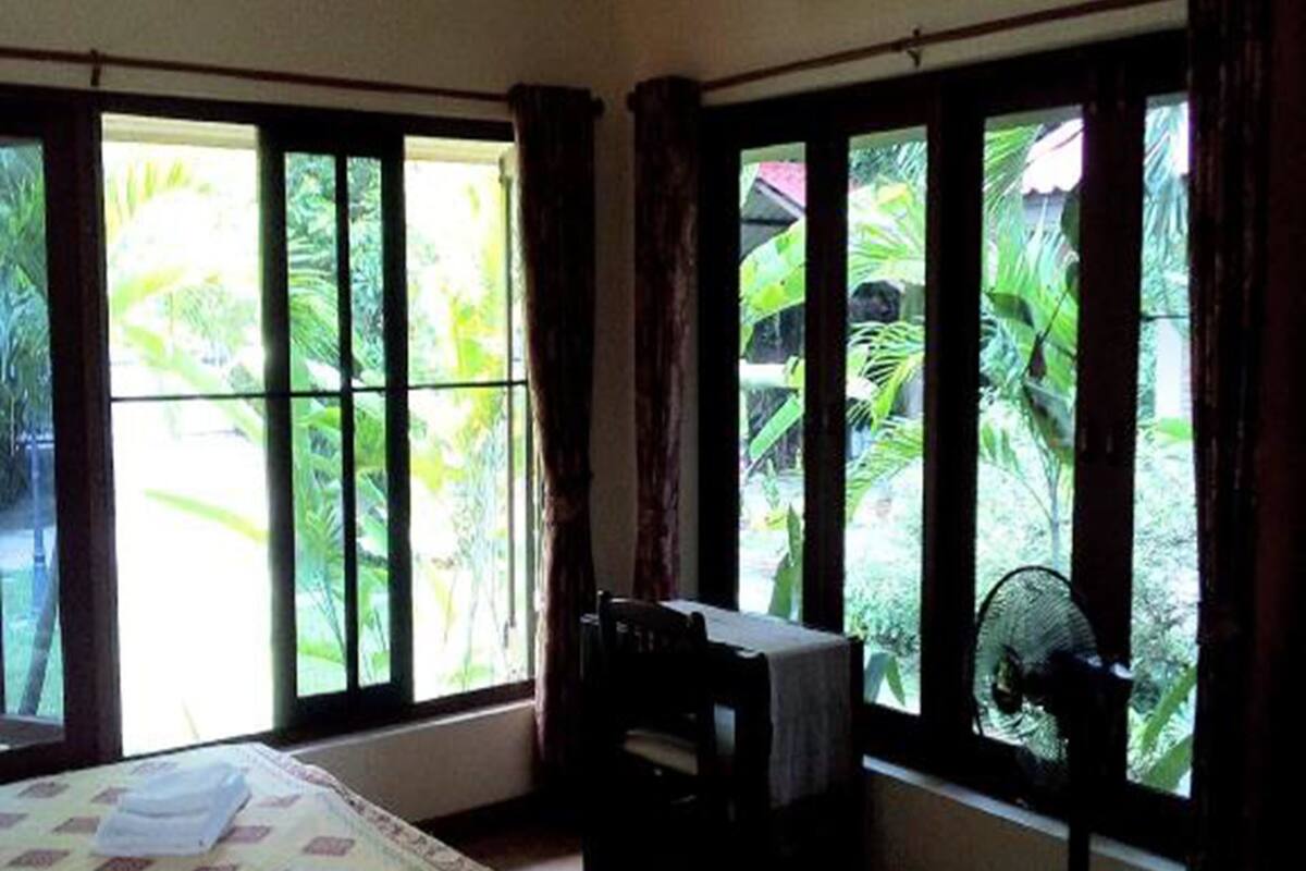 A room with a bed, a desk, and a window with a view of greenery.