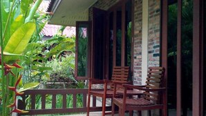 A covered porch with wooden chairs and a railing, surrounded by lush greenery. - Happy Garden villa (Krabi)