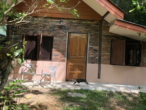 A brick house with a wooden door, a window with blinds, and a clear plastic chair outside.