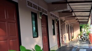 A covered corridor with red doors and tiled flooring, leading to a building entrance. - Levante (Surat Thani)
