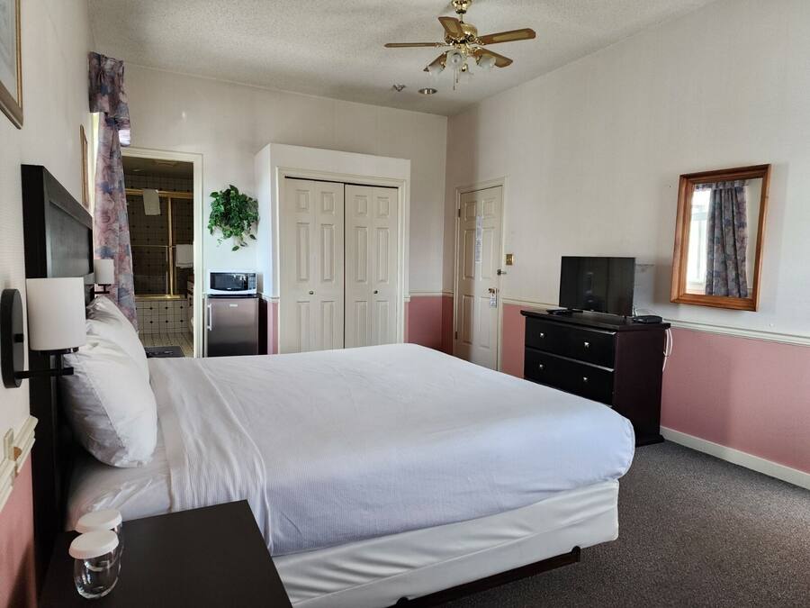 A hotel room with a bed, a TV, a desk, a microwave, a ceiling fan, and a door leading to a bathroom.