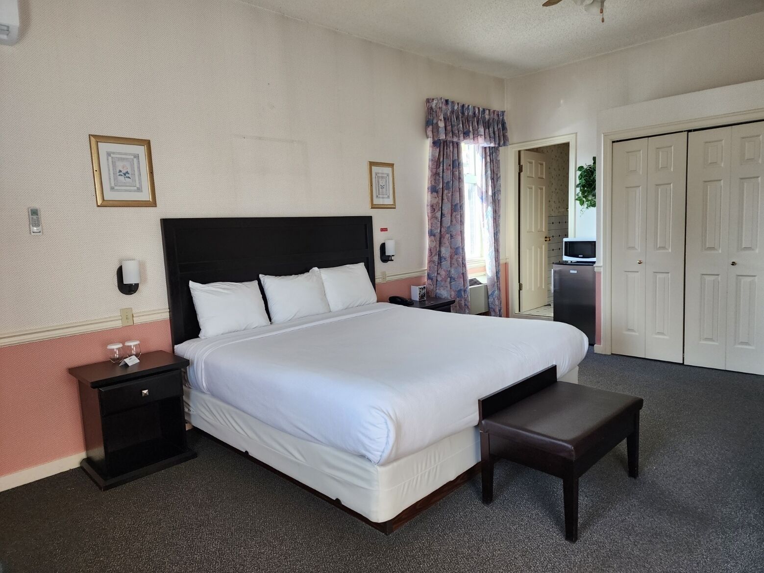 Een hotelkamer met een groot bed, een nachtkastje, een bankje, een televisie en een garderobe.