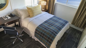 Une chambre d’hôtel avec un lit, un bureau avec un téléphone, une chaise, une lampe et une fenêtre avec des rideaux.