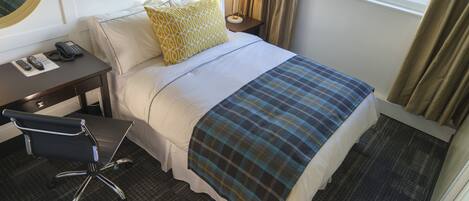 A hotel room with a bed, a desk with a telephone, a chair, a lamp, and a window with curtains.