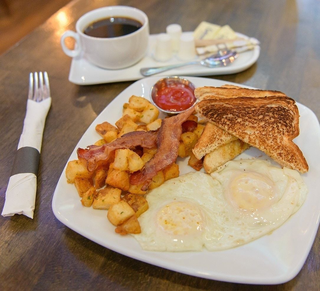 A plate of breakfast food including fried eggs, bacon, hash browns, toast, and a cup of coffee.