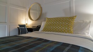 Een hotelkamer met een bed, een bureau, een stoel en een ronde spiegel aan de muur.