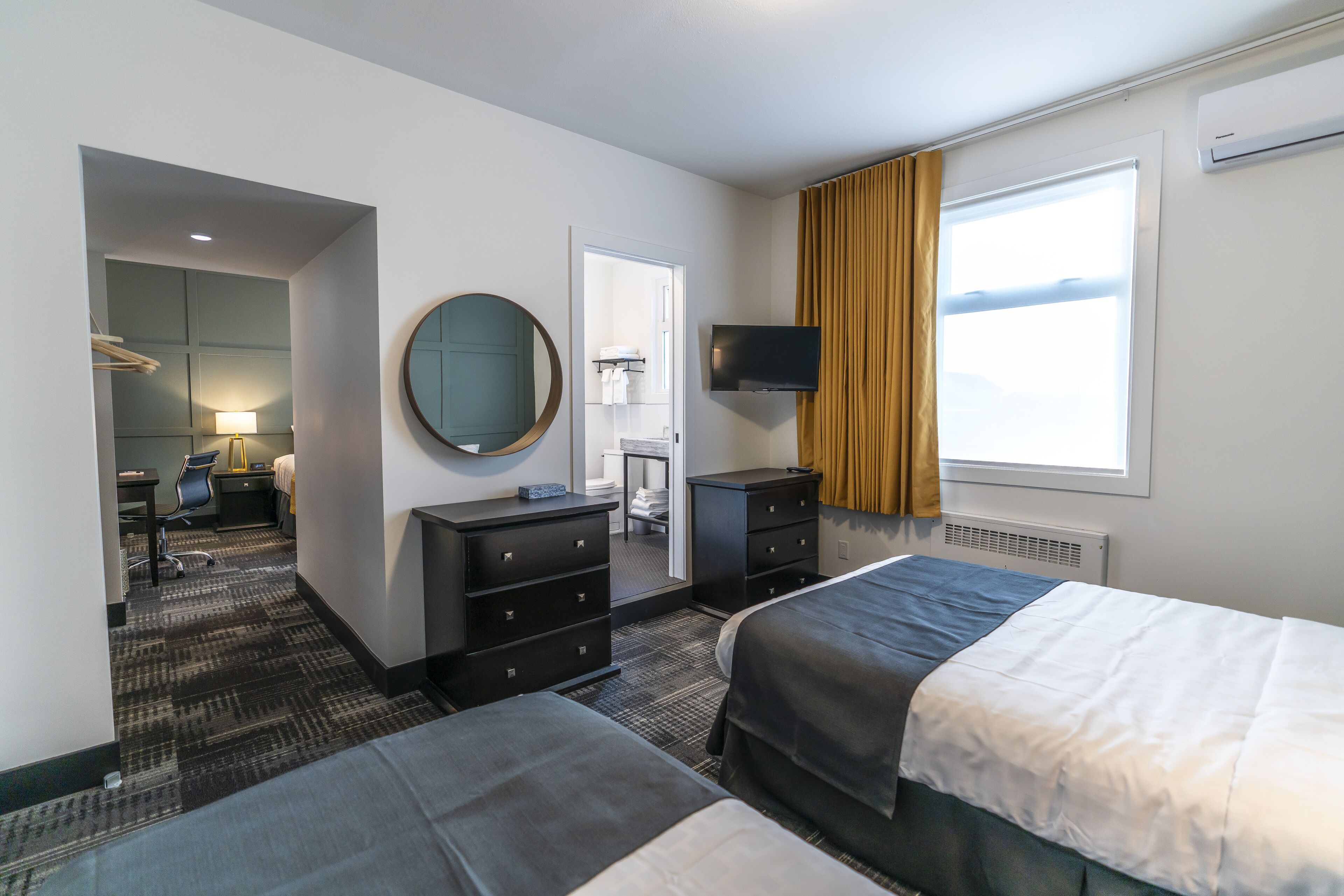 A hotel room with two beds, a desk, a chair, a TV, and a window with curtains.
