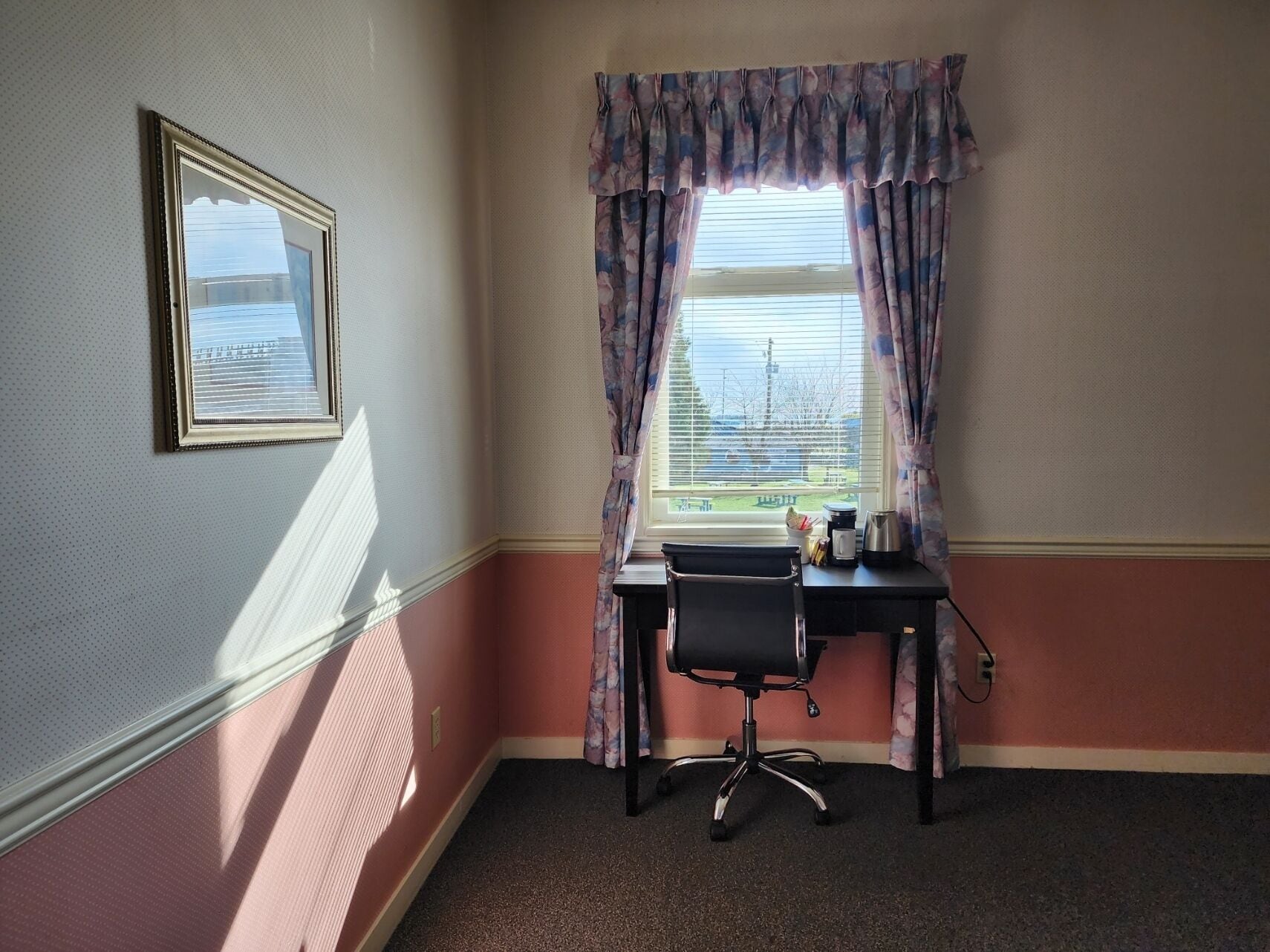 A corner room with a desk, chair, and window with curtains.
