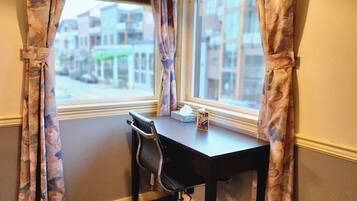 A corner office with a desk and chair, a window with curtains, and a hanging light fixture.