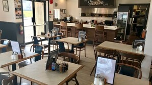 Een restaurant interieur met houten tafels en stoelen, een keukenhoek en een bord met de tekst 'The Steveston Cafe'.