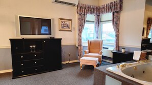 Hotelkamer met een flatscreen televisie, een zwarte dressoir, een roze fauteuil, een groot bad en een raam met gordijnen.