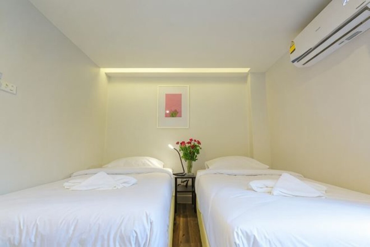 Habitación de hotel con dos camas, una mesita de noche, un florero con flores y un equipo de aire acondicionado.