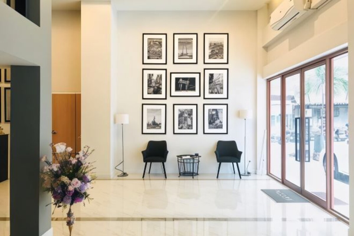 Un área de recepción con suelo de mármol, dos sillas negras, un jarrón de flores y una pared con fotografías blanco y negro enmarcadas.