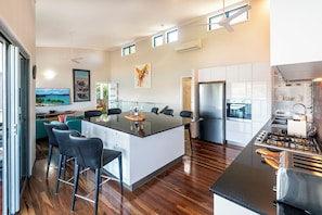 A modern kitchen with a central island, bar stools, and a dining area. - Casuarina Cove 16 Ocean View Deluxe Refurbished 3 Bedroom House Near Marina With Golf Buggy (Whitsundays)