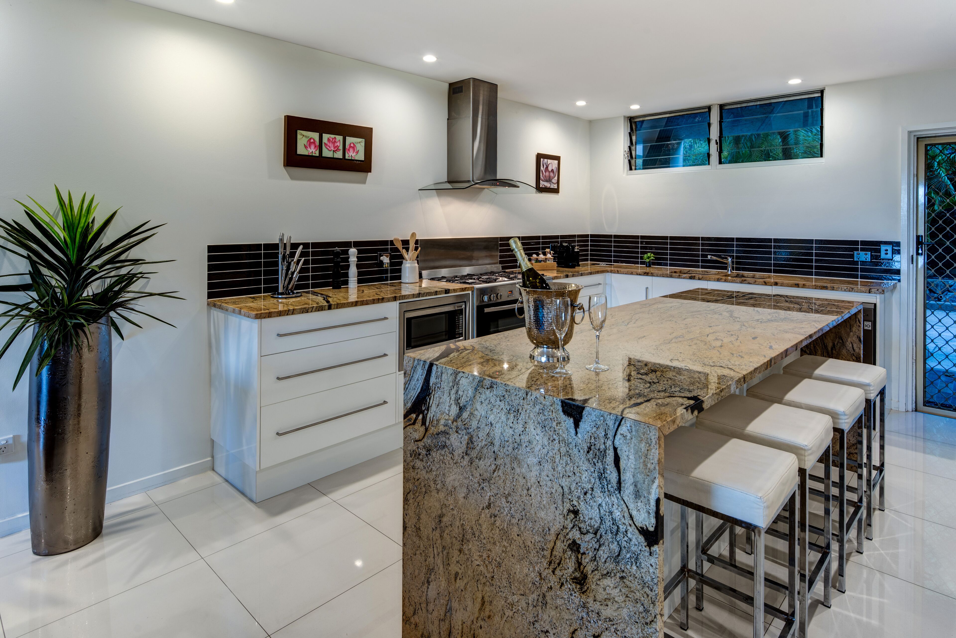 A modern kitchen with a large island, white cabinetry, and a stainless steel range hood.