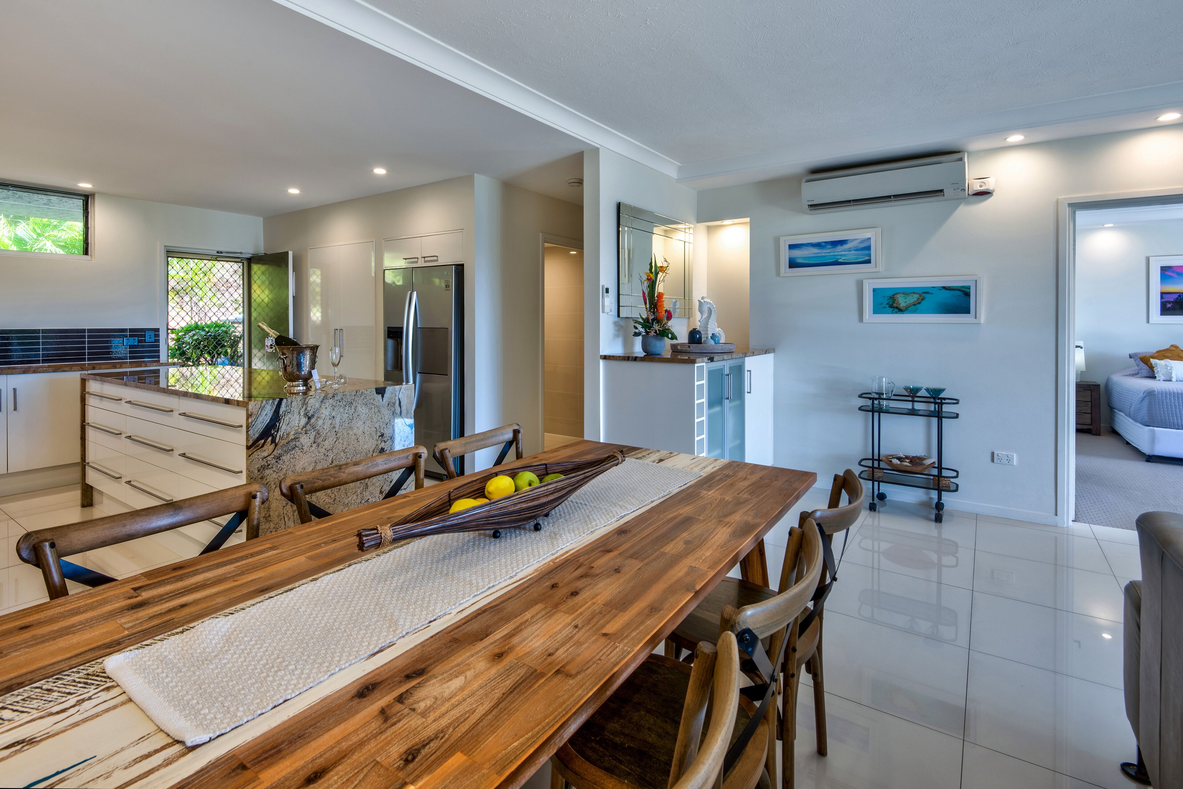 A modern kitchen with a wooden dining table, chairs, and a fruit bowl.
