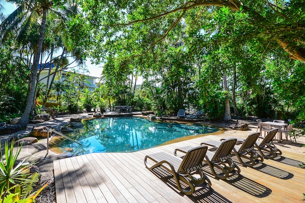 A wooden deck with lounge chairs and a swimming pool surrounded by lush greenery.