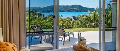 Ein Schlafzimmer mit einem großen Fenster mit Blick auf eine malerische Landschaft aus Wasser und Hügeln.