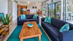 A modern living room with a sofa, coffee table, and a view of the kitchen and dining area. - Oasis 1 Hamilton Island 2 Bedroom Apartment In Central Location With Golf Buggy (Whitsundays)